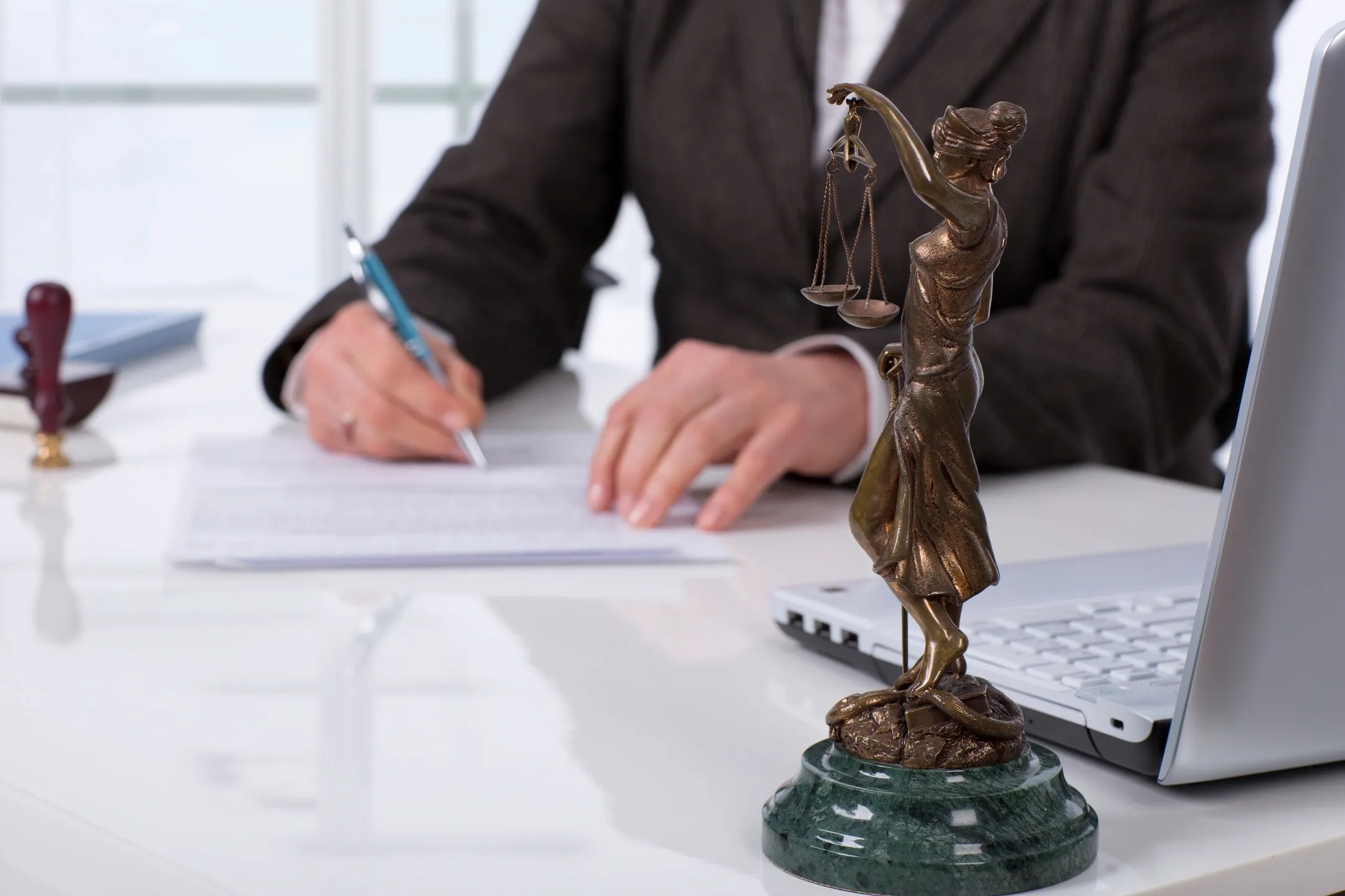 Justice statue on desk near person writing.