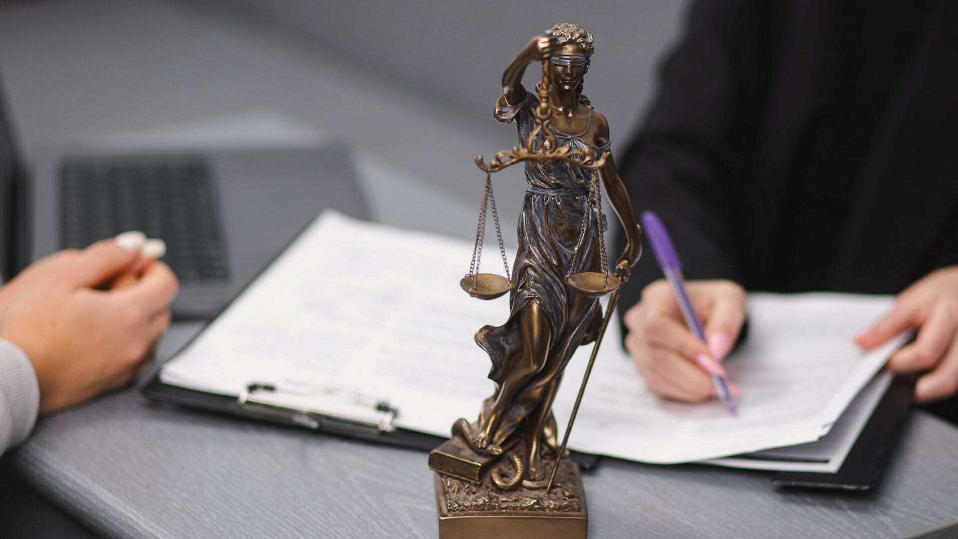 Lady Justice statue with people discussing documents.